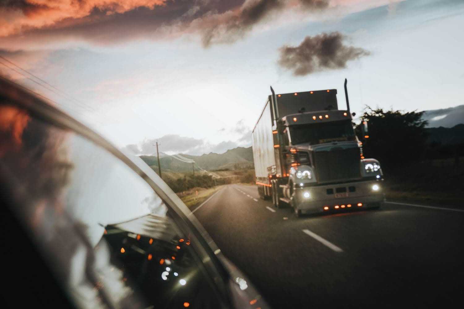 A semi truck on the highway under a dusk sky